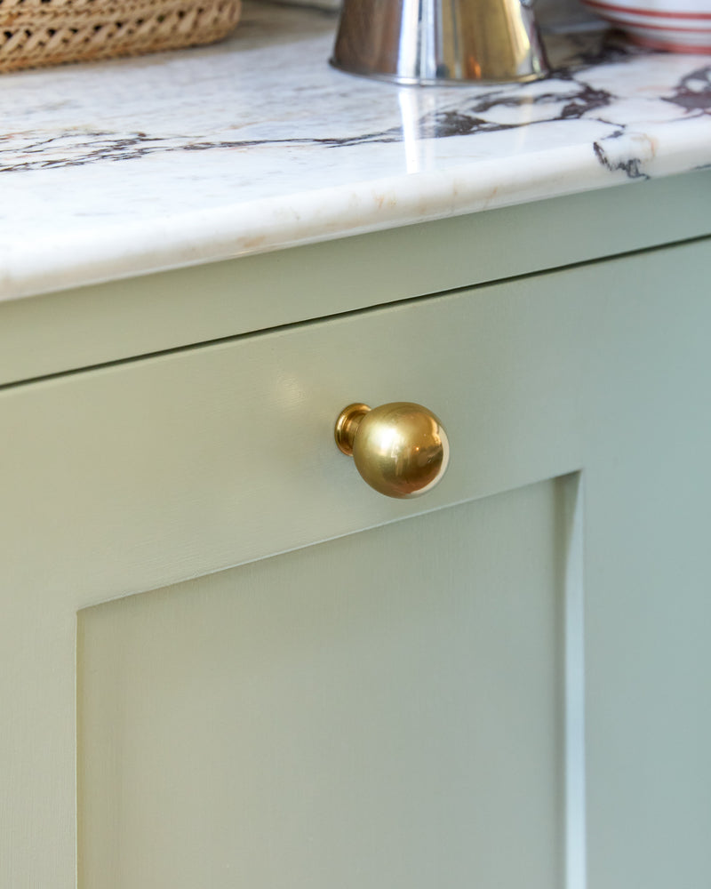 Light green cabinet with a brass knob on a marble countertop